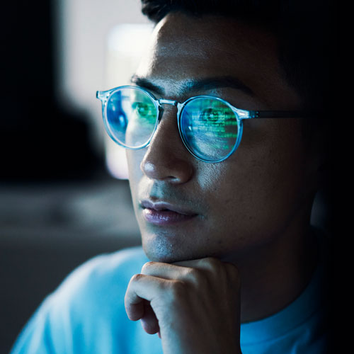 Closeup shot of an aisan man wearing glasses in which a string of green data is reflected