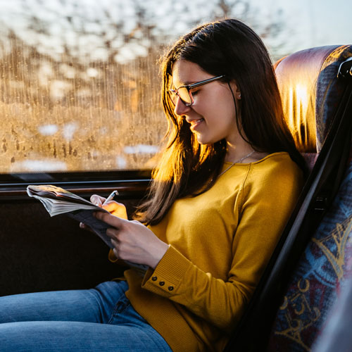 Woman in yellow jumper reading a magazine while travelling on a bus