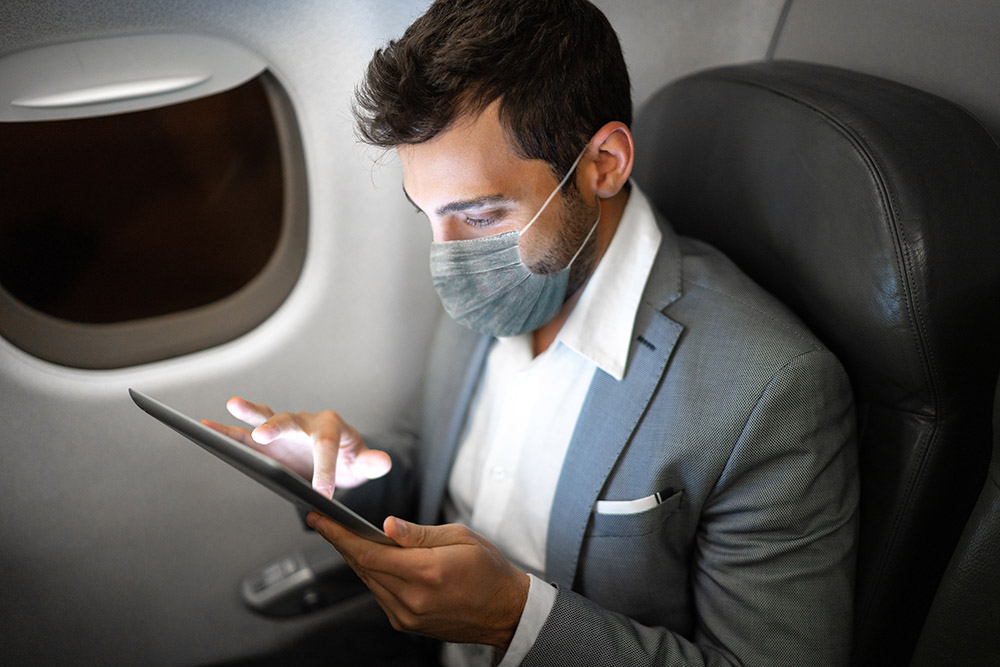 Businessman flying using digital tablet with protective mask business traveller keeps travelling