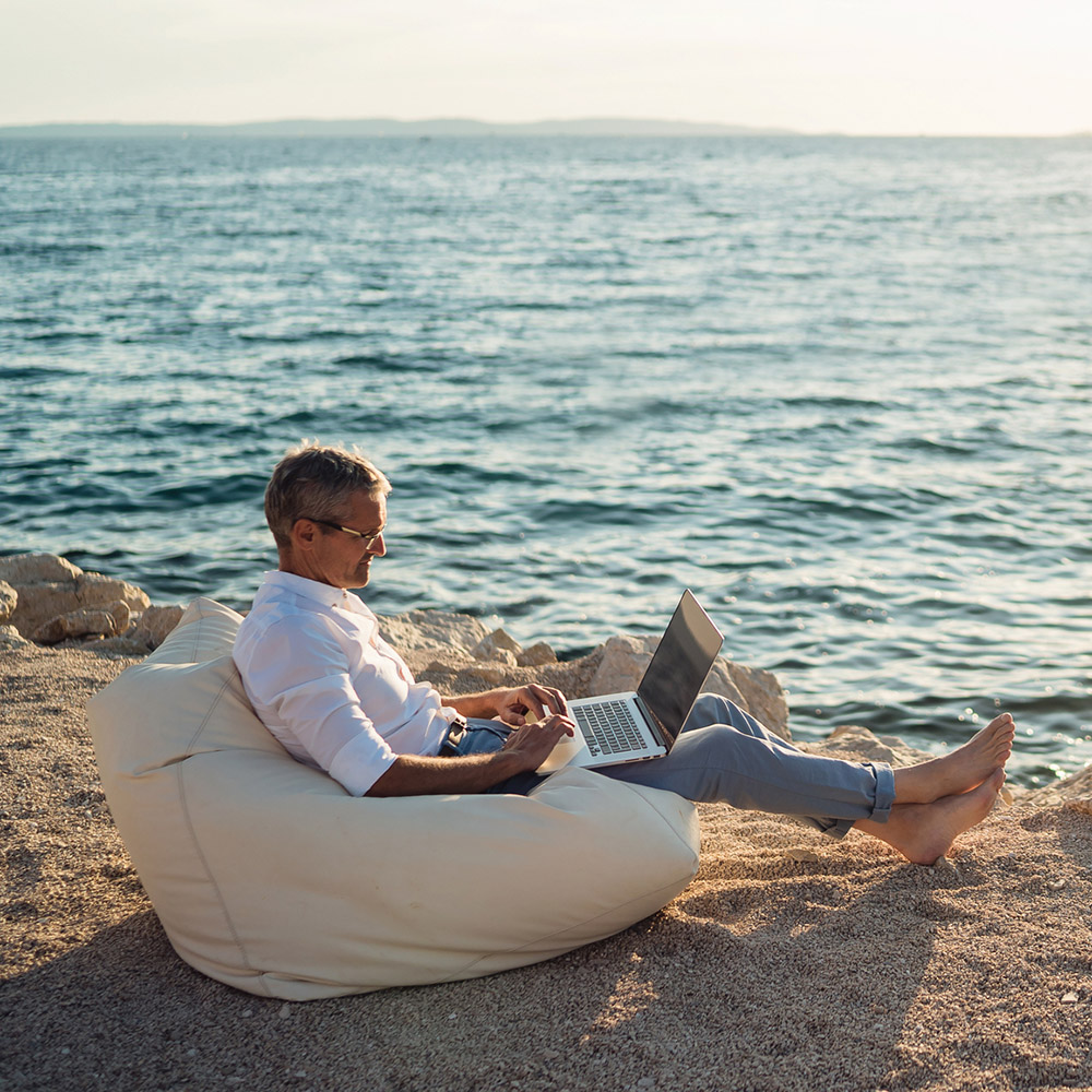 Senior man working on his laptop lying on deck chair on the beach Business Traveller working on the beach