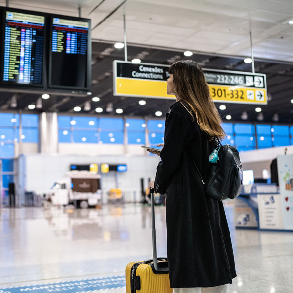 Young woman in black coat looking at the depature boards at an airport with a yellow roller case